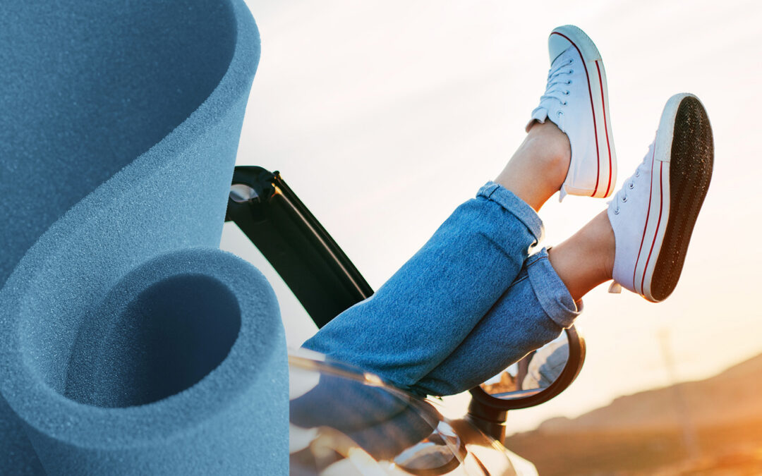 A roll of blue open cell PU foam to the left. To the right, a pair of legs in jeans wearing white sneakers raised over the door of a convertible
