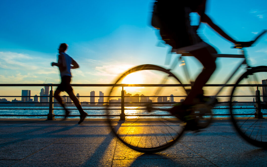 A jogger and a cyclist silhouetted against the sunset over a beach landscape.